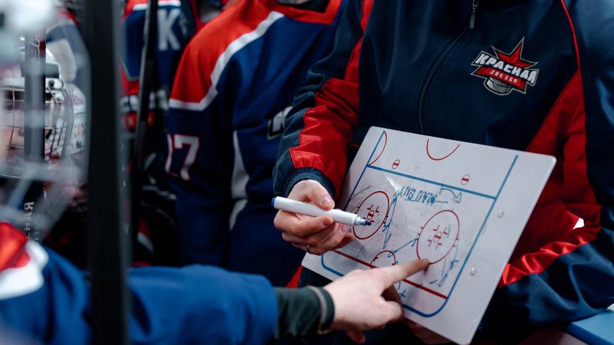 Hockey coach discussing tactics on a board with players during match break.